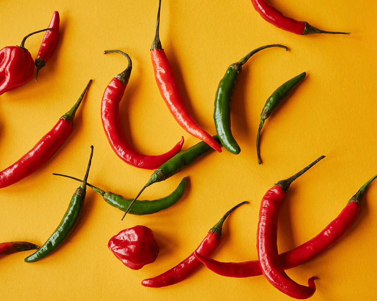 A collection of vibrant red and green chili peppers set on a yellow surface.