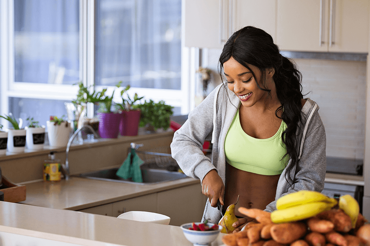 A person in workout gear chopping a pear next to an assortment of colorful fruits.