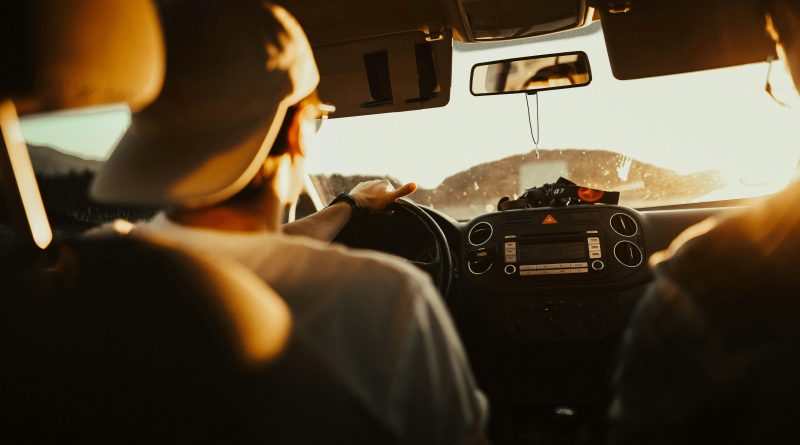 Two people in a car driving toward a bright sun.