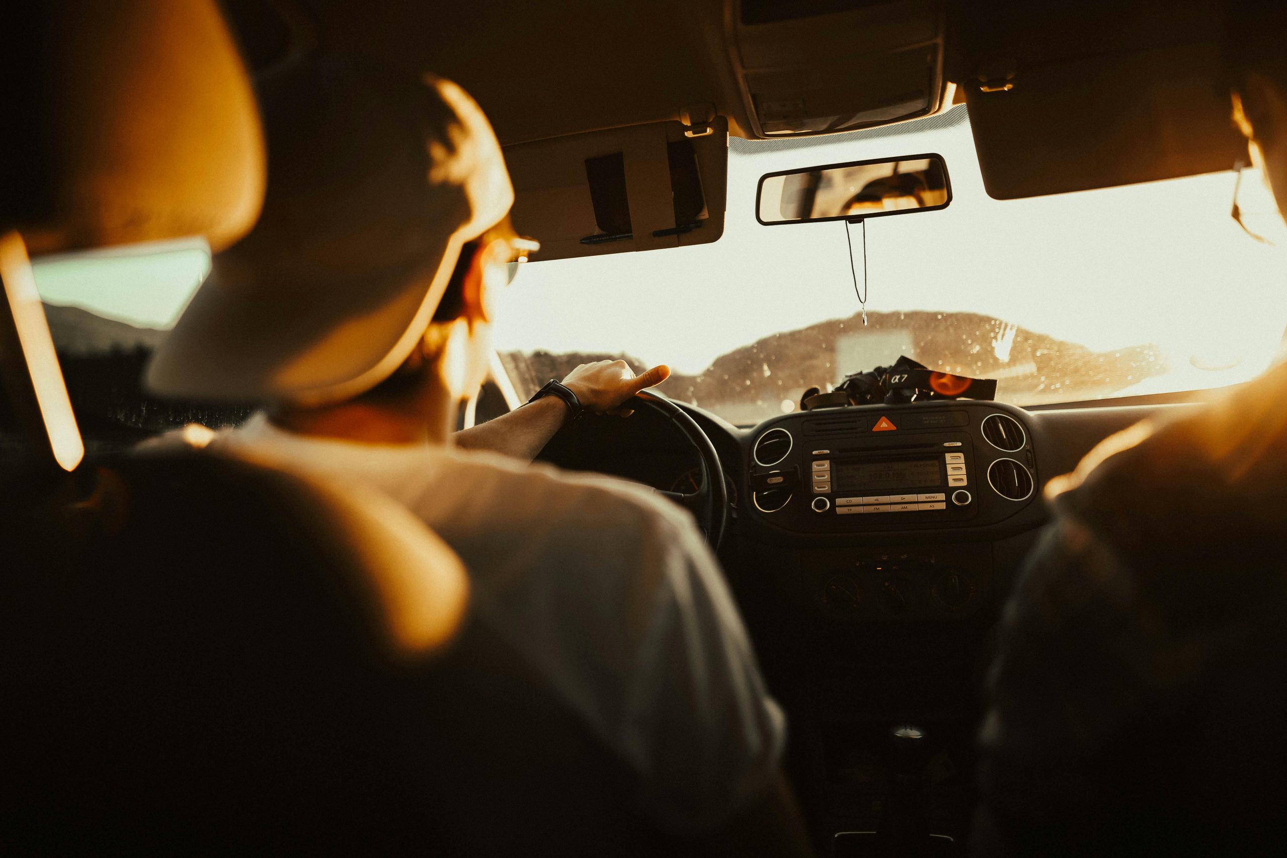 Two people in a car driving toward a bright sun.