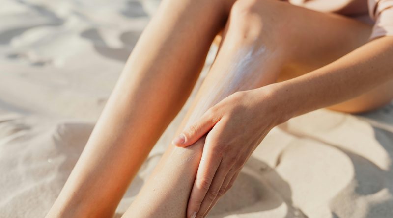 A person rubbing sunscreen onto their legs on a sandy beach.