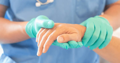 A gloved physician holding a patients hand while inspecting it.