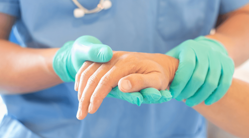 A gloved physician holding a patients hand while inspecting it.