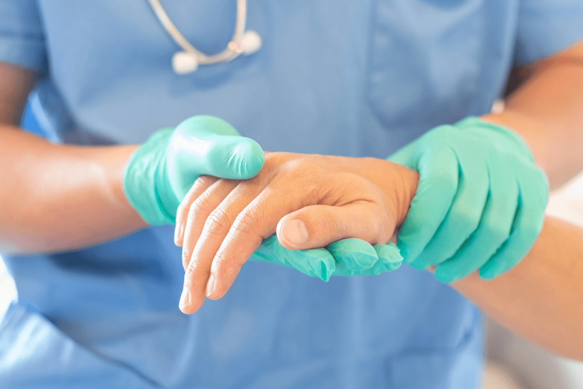 A gloved physician holding a patients hand while inspecting it.