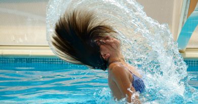 A person emerging from a pool while tossing their hair back, creating an arc of water.