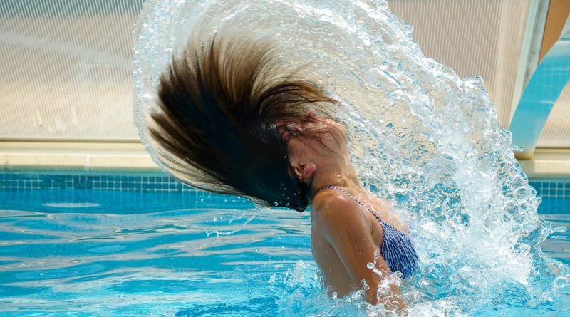 A person emerging from a pool while tossing their hair back, creating an arc of water.