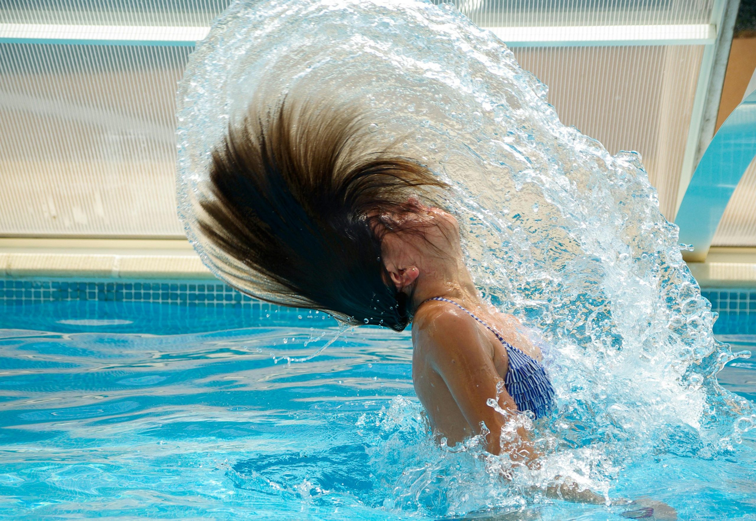 A person emerging from a pool while tossing their hair back, creating an arc of water.