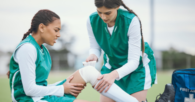 A soccer player helping another tape an injured knee on the field.