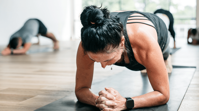 A person in a yoga pose, propped up on their elbows while facing the mat.