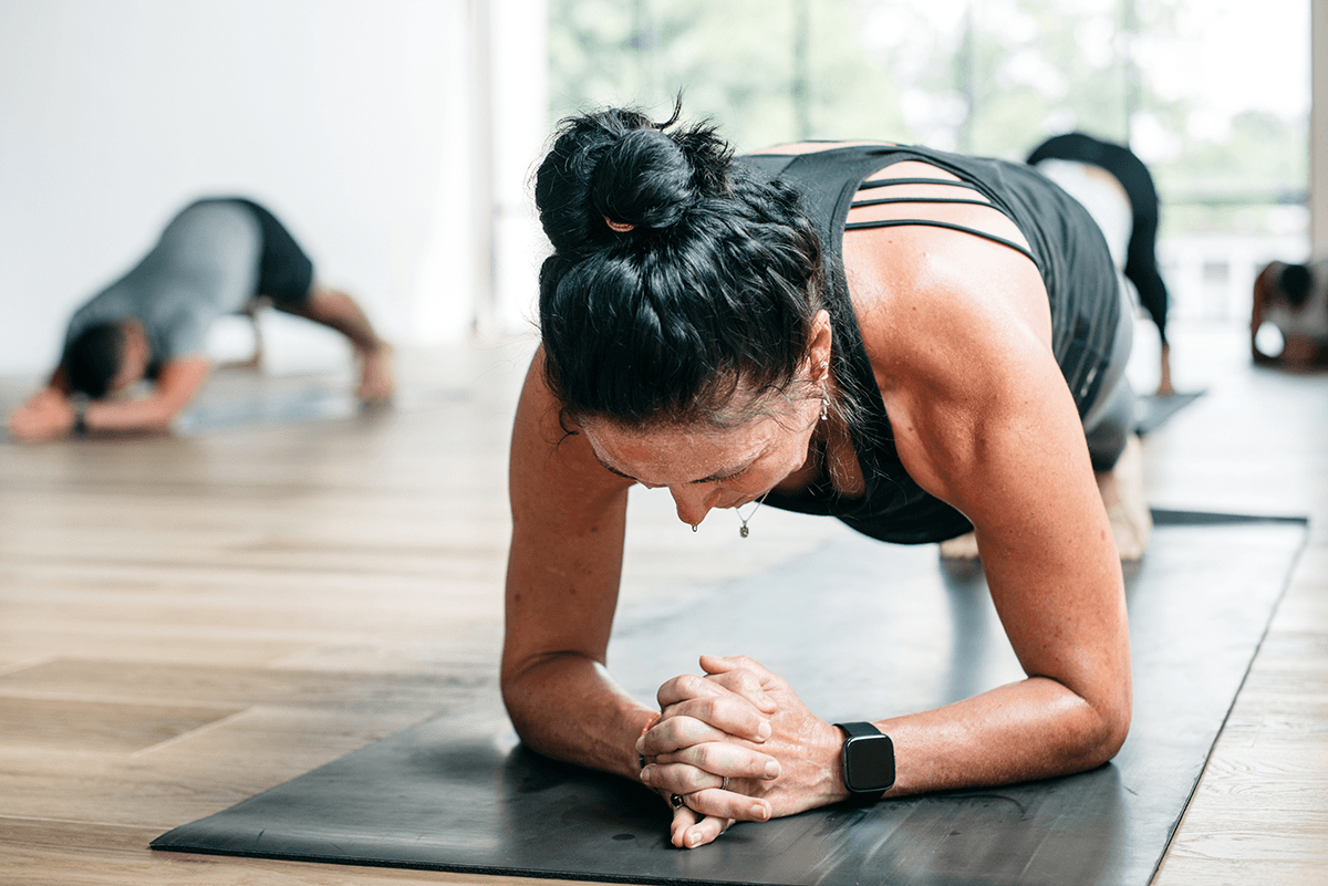 A person in a yoga pose, propped up on their elbows while facing the mat.