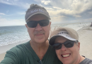 Elton Youngblood and his wife smiling on a bright beach.