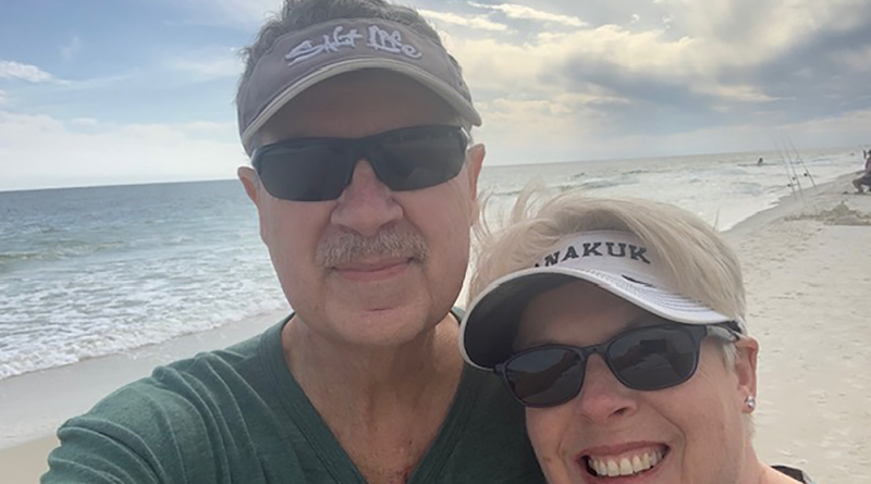 Elton Youngblood and his wife smiling on a bright beach.