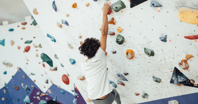 A person reaching up to a handhold while bouldering up a wall.