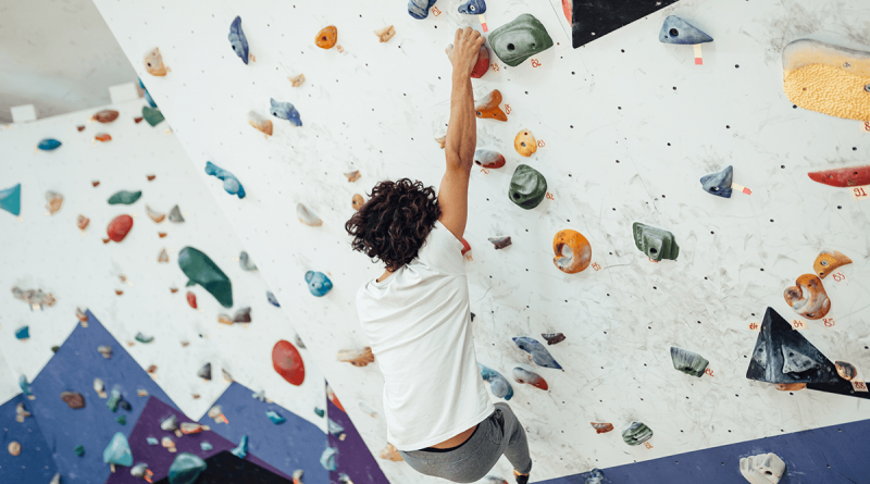 A person reaching up to a handhold while bouldering up a wall.