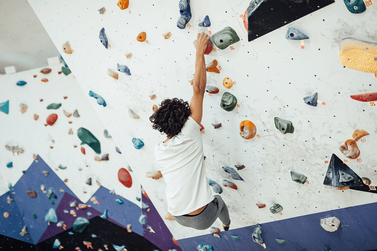 A person reaching up to a handhold while bouldering up a wall.