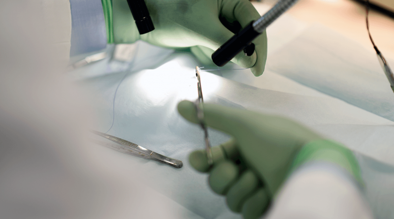 Green-gloved hands manipulating sutures on a patient.