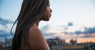 A black woman with long braids outside looking across the horizon.