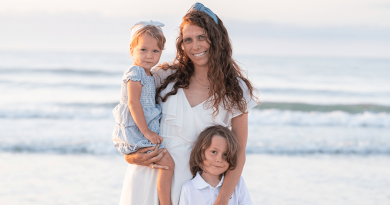 A smiling woman on a beach with two children.