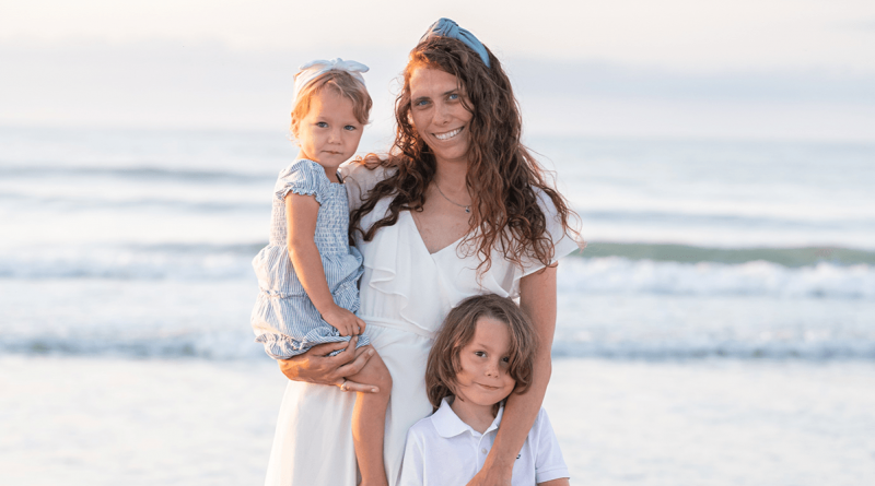 A smiling woman on a beach with two children.