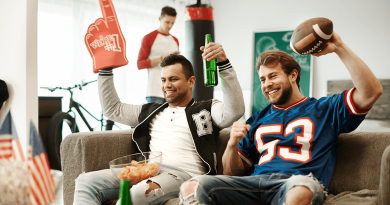 Two football fans on a coach cheering while a third snacks in the background.