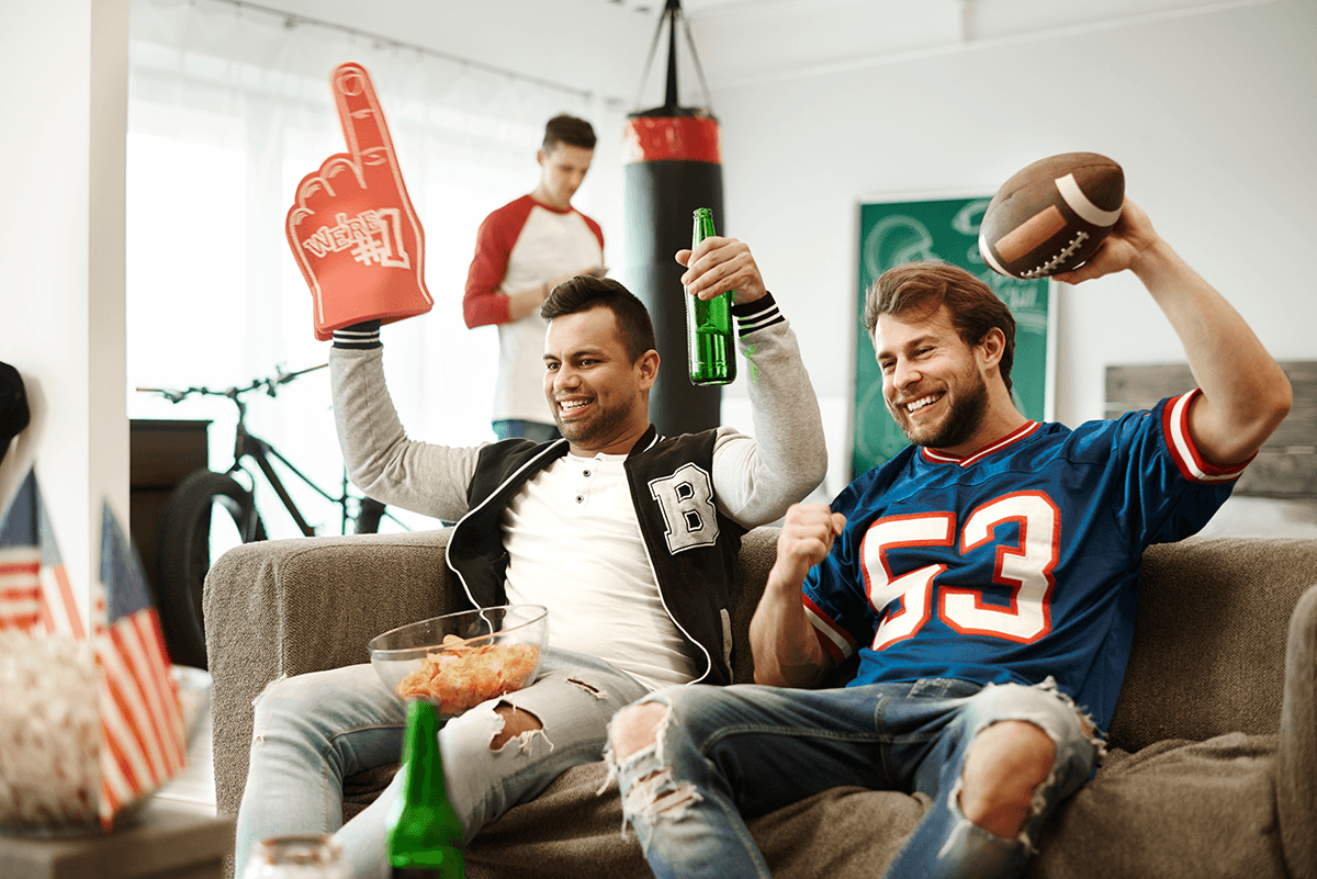 Two football fans on a coach cheering while a third snacks in the background.