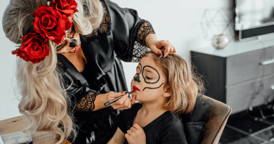 An adult using costume makeup to paint a skull face onto a child.