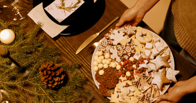 A person placing a tray of colorful holiday cookies onto a festive table.