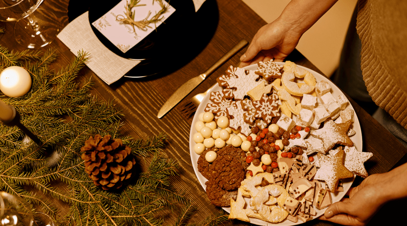 A person placing a tray of colorful holiday cookies onto a festive table.