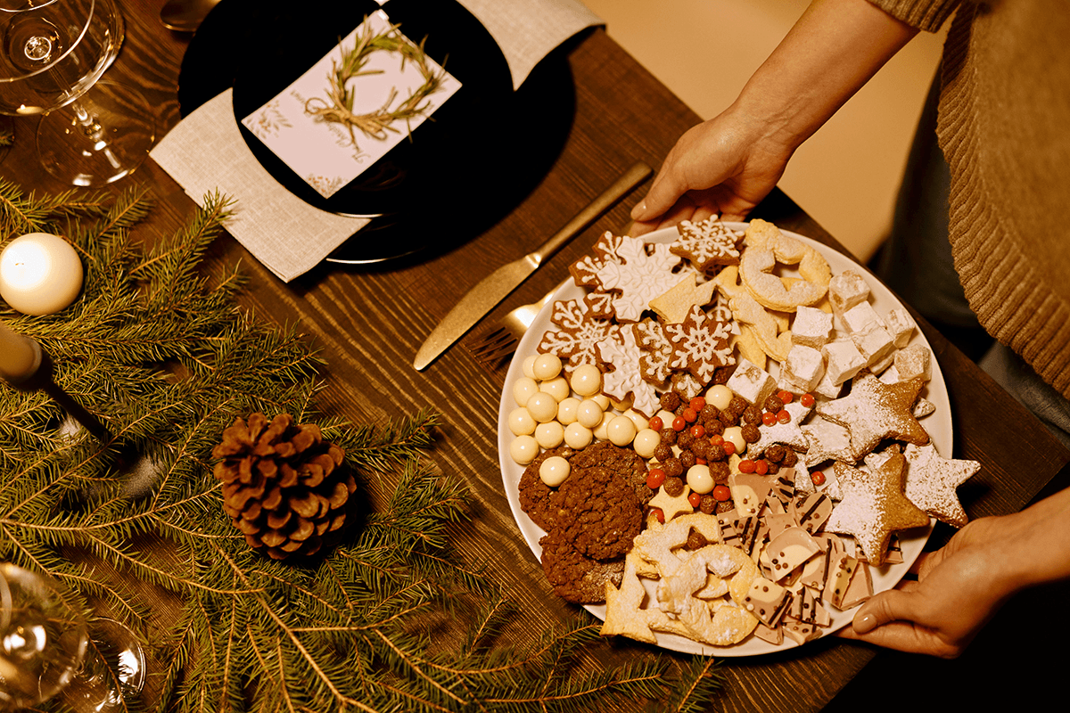 A person placing a tray of colorful holiday cookies onto a festive table.