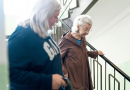 An older adult being helped down a flight of stairs by another adult.