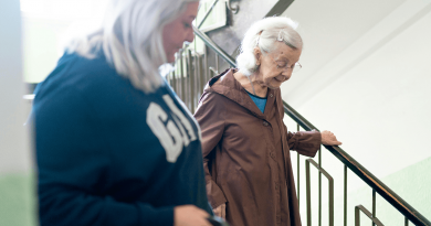 An older adult being helped down a flight of stairs by another adult.