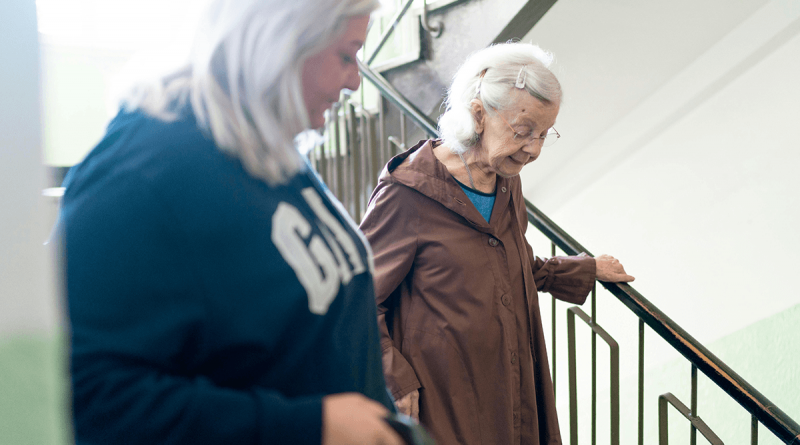 An older adult being helped down a flight of stairs by another adult.