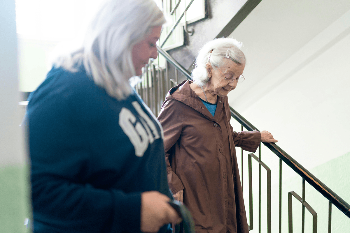 An older adult being helped down a flight of stairs by another adult.