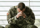 A soldier sitting on a bench with his head buried in his hands.