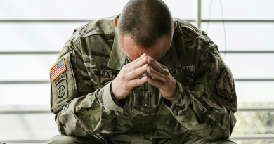 A soldier sitting on a bench with his head buried in his hands.