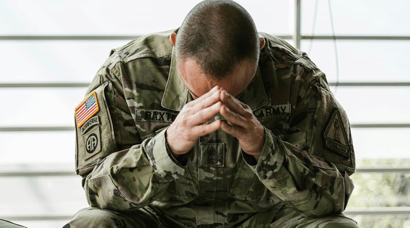 A soldier sitting on a bench with his head buried in his hands.