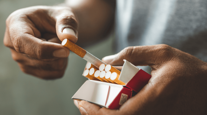 A pair of hands pulling a cigarette out of a pack.