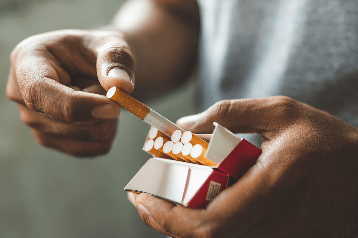 A pair of hands pulling a cigarette out of a pack.