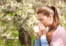 A woman with a long ponytail sneezing into a tissue while outside.