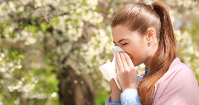 A woman with a long ponytail sneezing into a tissue while outside.