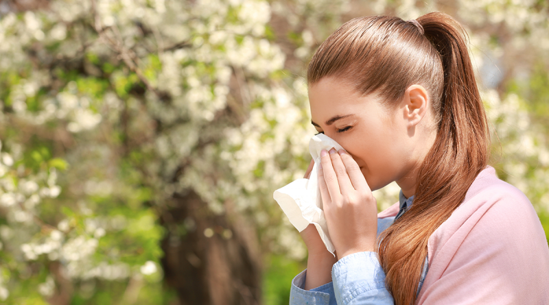 A woman with a long ponytail sneezing into a tissue while outside.