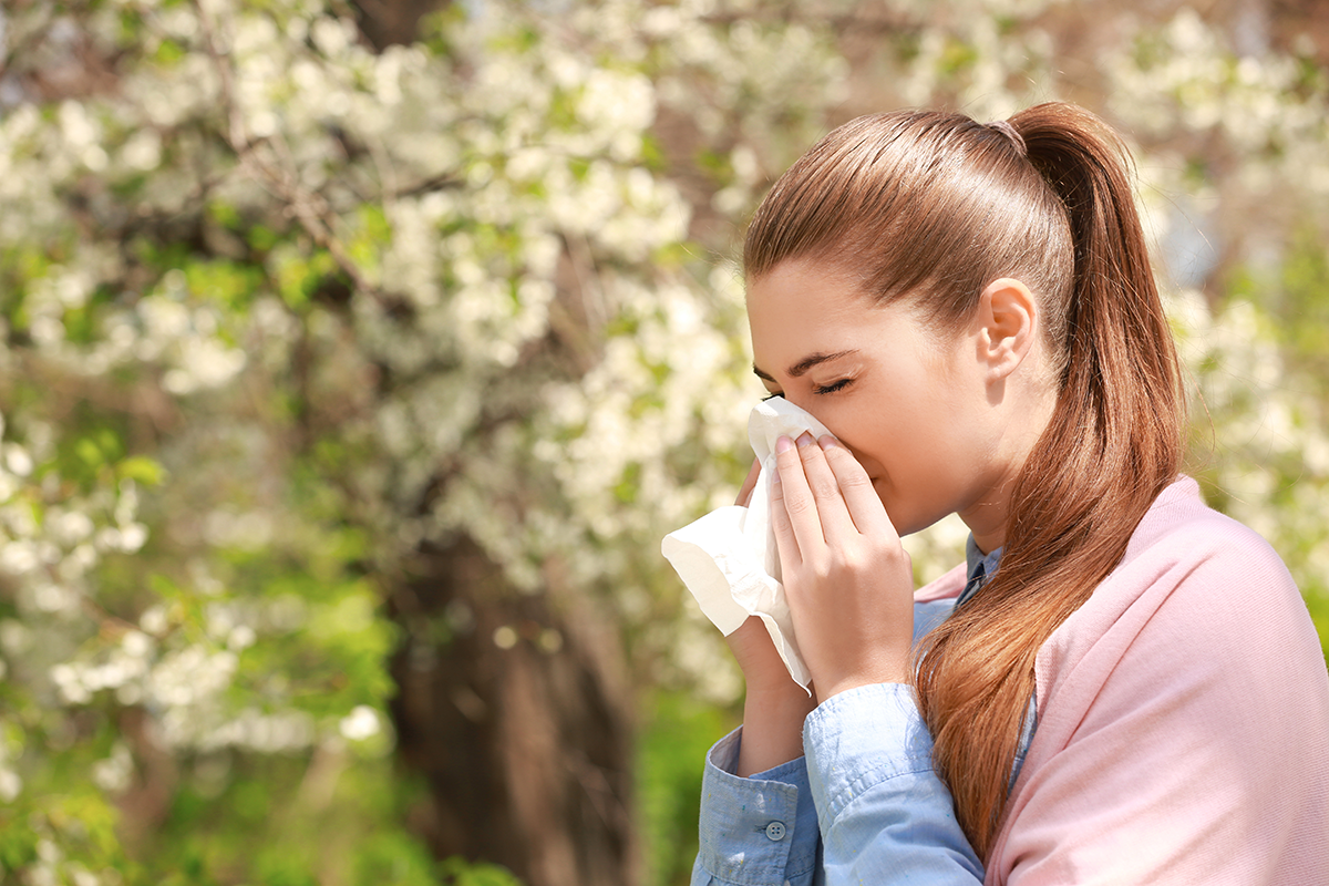 A woman with a long ponytail sneezing into a tissue while outside.