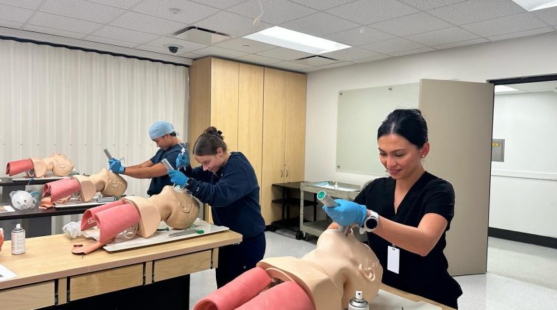 Three students practicing breathing assistance with mannequins.