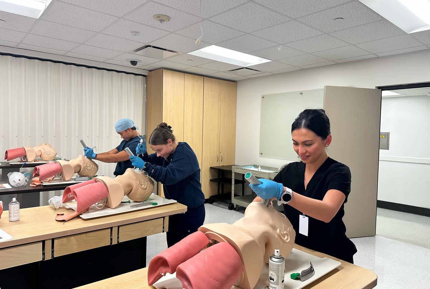 Three students practicing breathing assistance with mannequins.