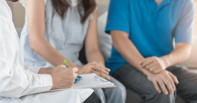 Two people seated with a doctor who is writing notes on a clipboard.