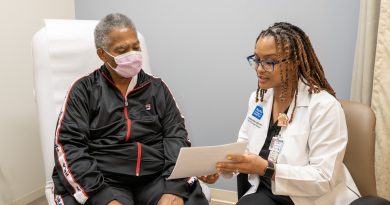 Elexis Williams showing a patient an information packet. The patient wears a black jacket and a face mask.