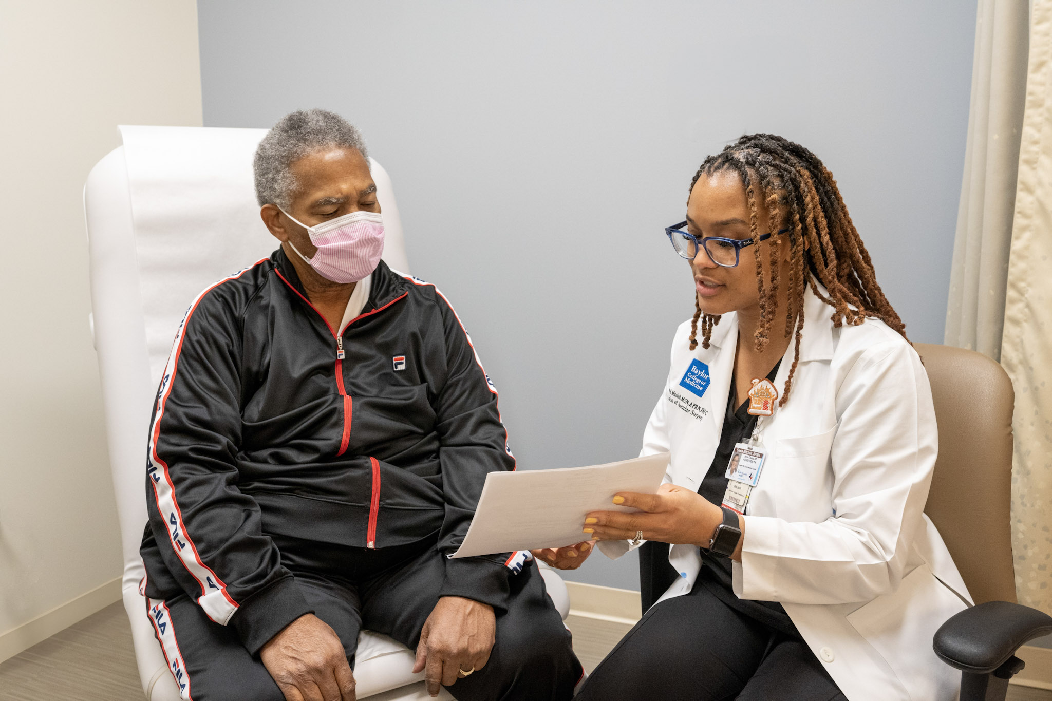 Elexis Williams showing a patient an information packet. The patient wears a black jacket and a face mask.