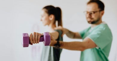 A trainer standing behind a person who is lifting a weight. The lifter holds a purple dumbbell stretched straight to their side, while the trainer guides their arm.