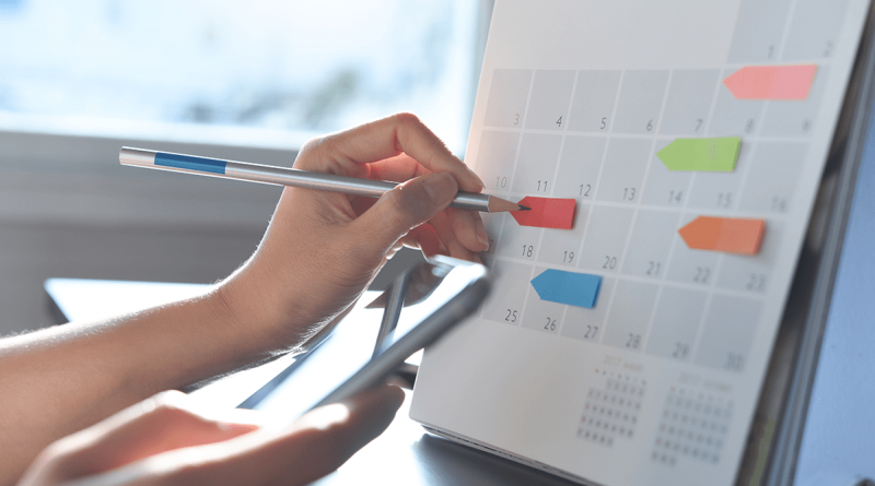 A person marking a desk calendar with sticky note arrows as labels.