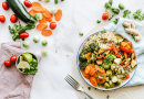 A vibrant and colorful salad made of carrot slices, cherry tomatoes, broccoli, squash, brussels sprouts and couscous.